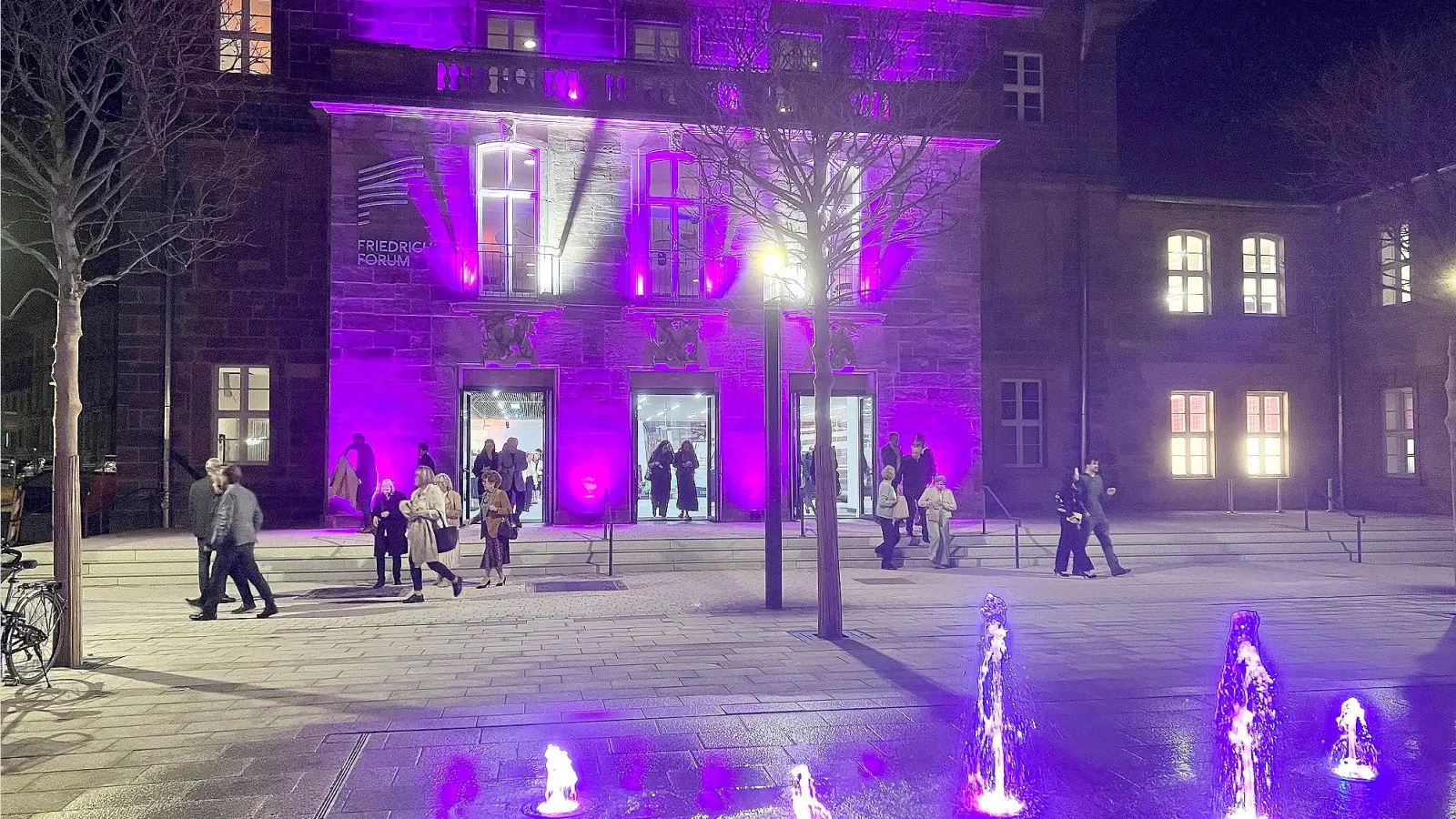 In violettes Licht getaucht präsentiert sich das Friedrichsforum am Abend: Vor der neu inszenierten Fassade versammelt sich das Publikum. Der neu geschaffene Brunnen belebt den Vorplatz. (Foto: W.Munzert)