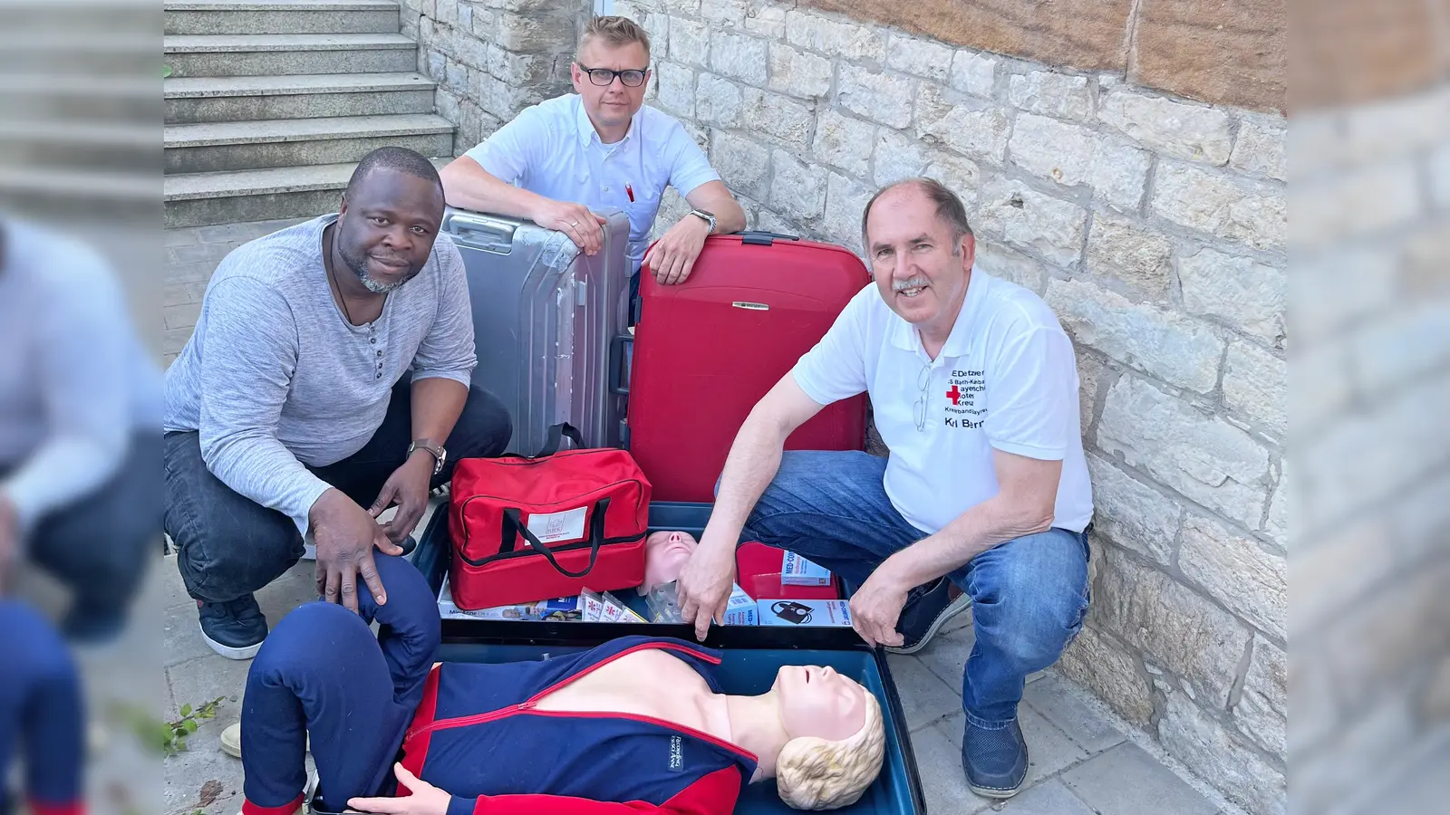 Reanimations-Dummy „Anne“ macht sich auf die Reise. V.l.: Prinz Ibukun Koussemou (Integrationsbeauftragten der Stadt<br>Bayreuth), Markus Ruckdeschel (Kreisgeschäftsführer des BRK-Kreisverbandes Bayreuth) und Karl Bernet (Projektkoordinator des Defi-Netzwerks der Integrierten Leitstelle Bayreuth/Kulmbach). (Foto: BRK Bayreuth)